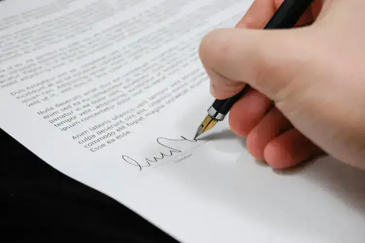 Company Formation FAQs – Infinite Corporate: close-up of a hand signing company documents with a fountain pen, representing filings and incorporation.